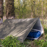 Bushmen Thermo Tarp 2x3 Olive set up in a forest, showcasing its water-resistant and thermal insulation features.