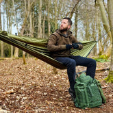 Man relaxing in a DD Recycled Camping Hammock in a forest, showcasing outdoor comfort and sustainability.