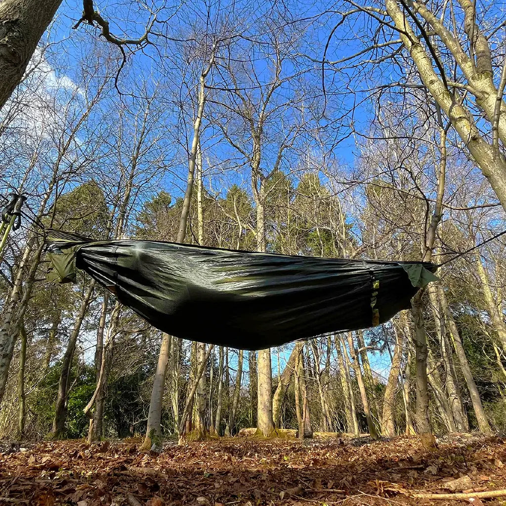 DD Recycled Frontline Hammock suspended between trees in a forest, made from recycled plastic bottles. DD Recycled Frontline Hammock suspended between trees in a forest, made from recycled plastic bottles.