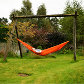 Person relaxing in a DD Chill Out Hammock on a swing set in a garden, surrounded by greenery.