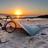 DD SuperLight Bikepacker Tarp set up at sunset on the beach with a bike nearby, ideal for adventurous camping.