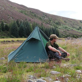 Man relaxing beside the DD Superlight Pathfinder Tent in a scenic wilderness setting.