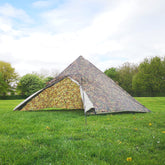 DD Pyramid Tent set up in a grassy field, showcasing camouflage design for outdoor shelter.