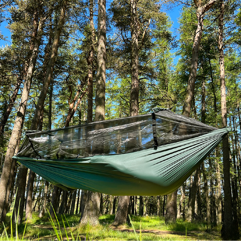 DD Superlight Frontline Hammock hanging in a serene forest setting, showcasing its lightweight design and mesh cover. DD Superlight Frontline Hammock hanging in a serene forest setting, showcasing its lightweight design and mesh cover.