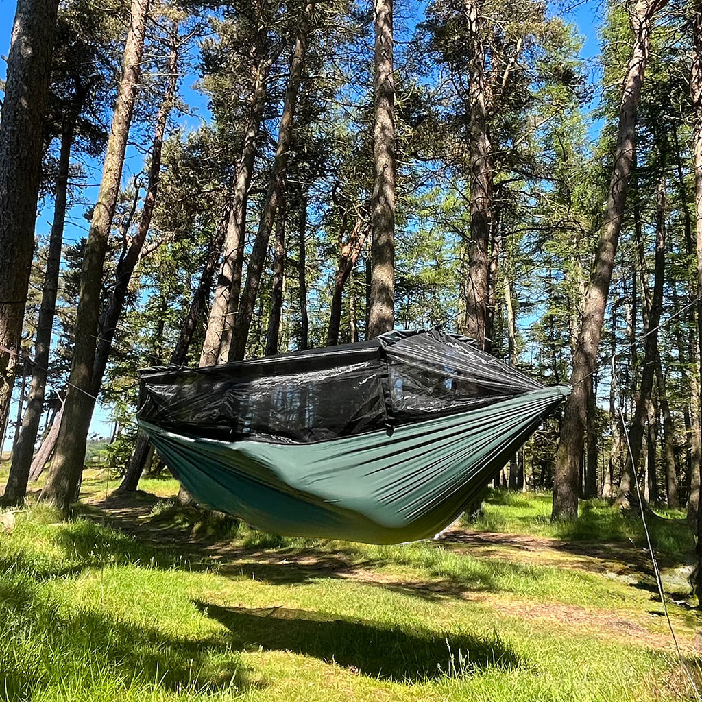 DD Superlight Frontline Hammock suspended in trees, featuring a lightweight design and mesh cover for outdoor adventures. DD Superlight Frontline Hammock suspended in trees, featuring a lightweight design and mesh cover for outdoor adventures.