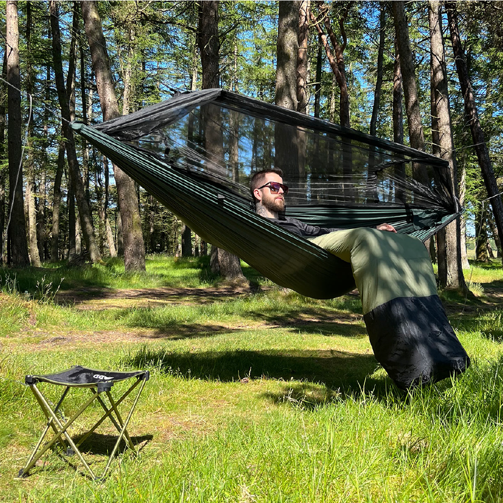 Man relaxing in a DD Superlight Frontline Hammock with integrated bug net in a forest setting. Man relaxing in a DD Superlight Frontline Hammock with integrated bug net in a forest setting.
