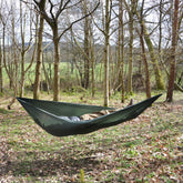 Person relaxing in a DD Superlight Hammock among trees in a serene outdoor setting.