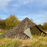 DD Tarp 3.5 x 3.5 in a camouflage pattern set up in a grassy field under a blue sky.