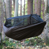 DD Frontline Hammock in a forest, features built-in mosquito net and durable double-layered design for outdoor comfort.