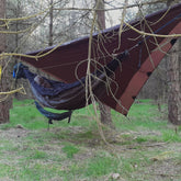 Person relaxing in a hammock under a DD Superlight Tarp in a forest setting, showcasing outdoor gear by DD Hammocks.