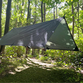 DD Tarp 2x2 hung between trees in a forest, providing weather protection for outdoor adventures.