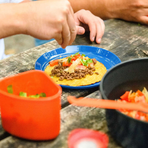Person preparing a taco on a blue plate with ingredients on a stone surface