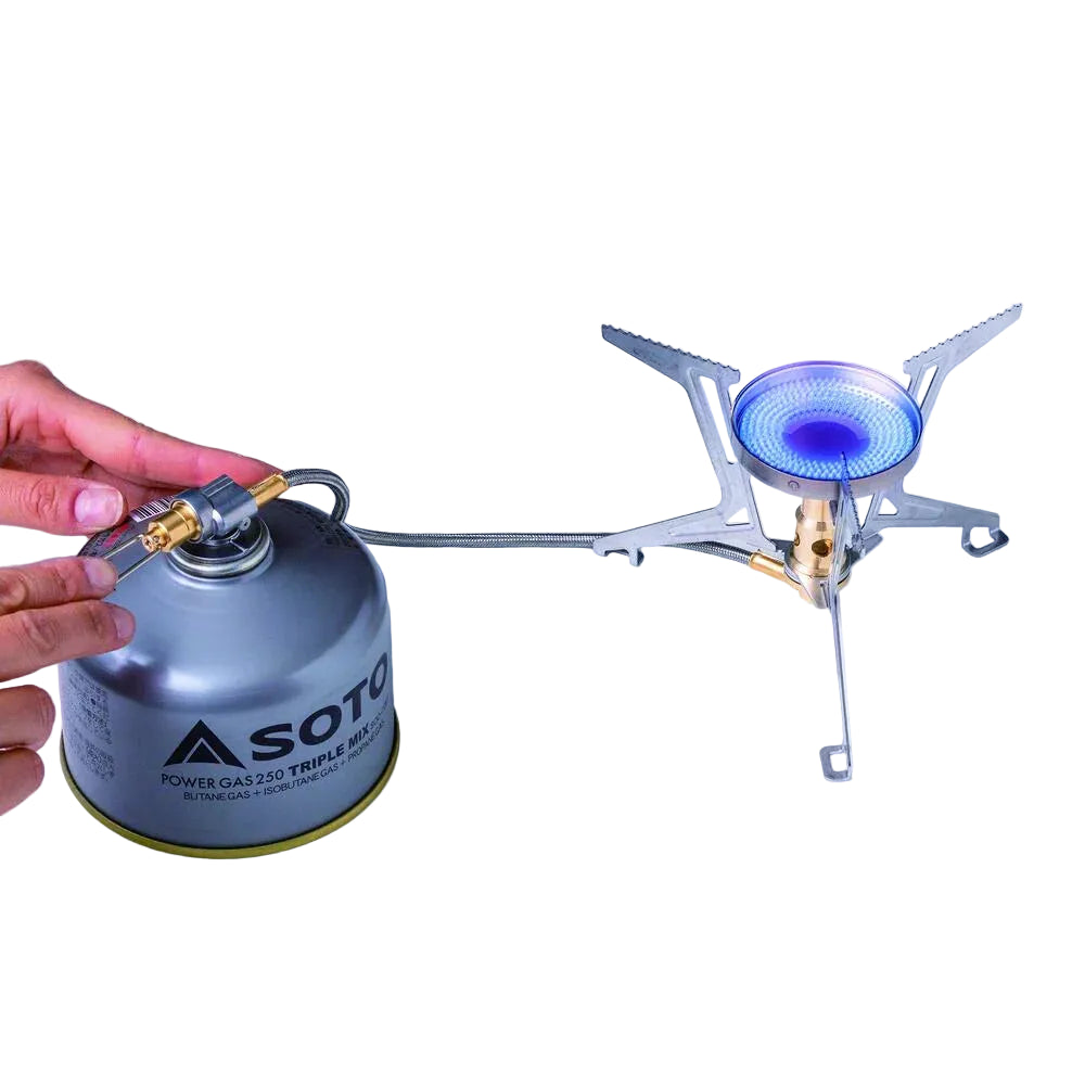Hand holding a Soto gas canister next to a portable stove with a blue flame on a white background