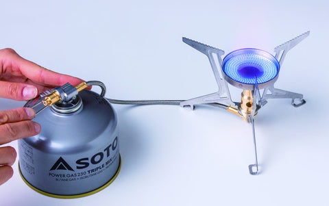 Hand holding a Soto gas canister to a camping stove on a white background