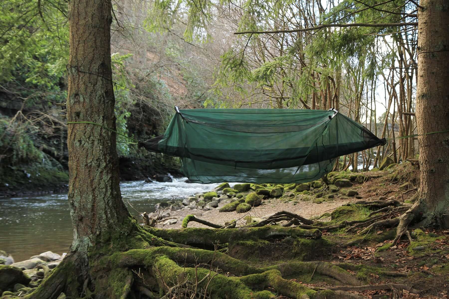 DD Hammock Mosquito Net set up between trees near a serene river, providing insect protection for camping.
